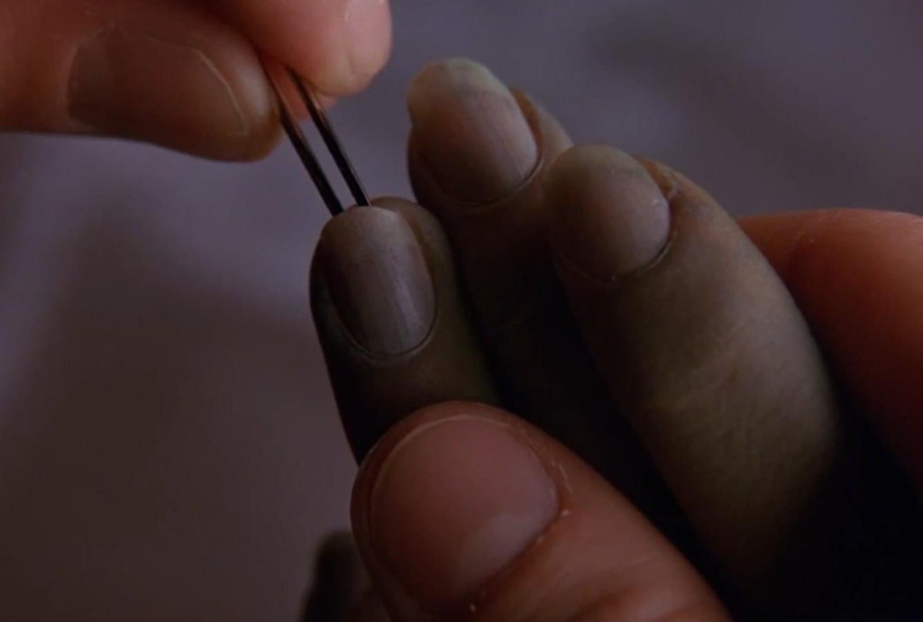 Tweezers lifting a tiny letter from under a fingernail