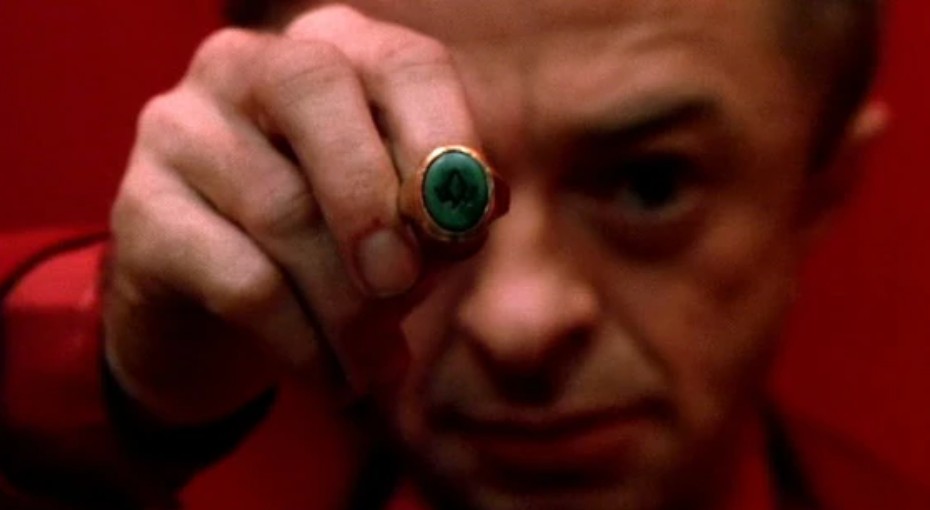 Owl Cave ring held before a face against red curtains