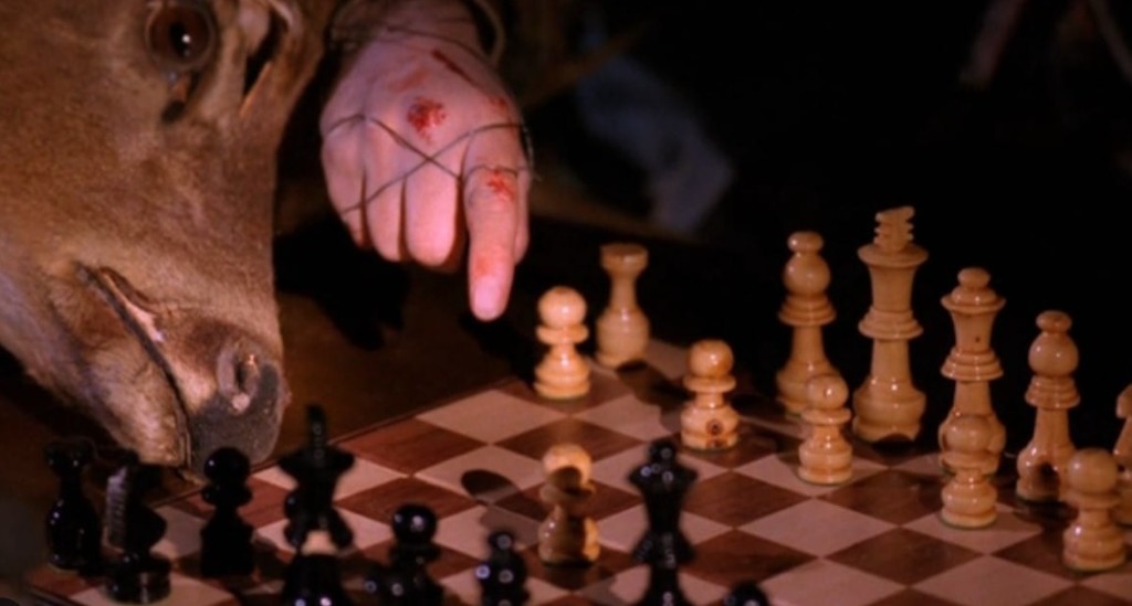 Wired hand pointing at a chess pawn; deer head beside the board
