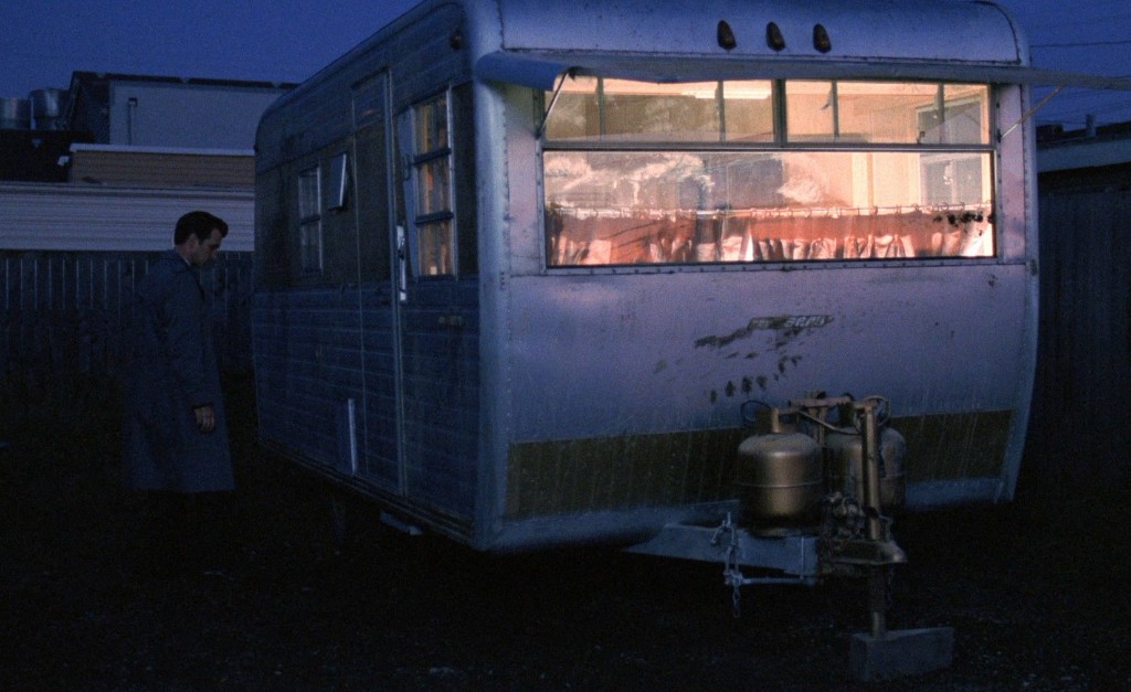 Chet Desmond at Fat Trout Trailer Park at night - lit trailer window, agent in coat