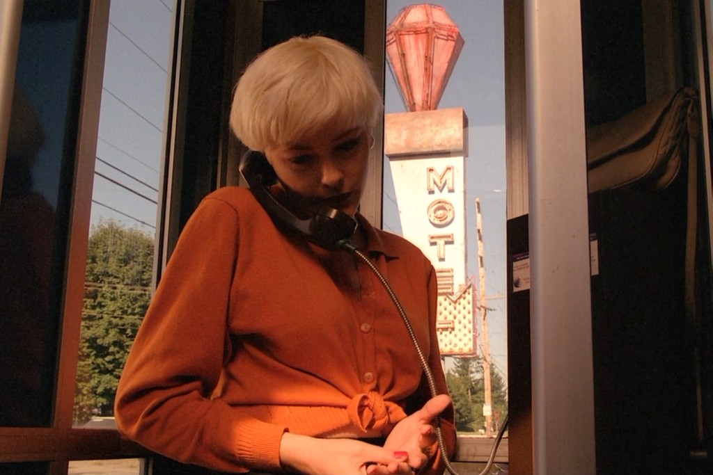 Teresa Banks in a phone booth at dusk - motel sign behind her