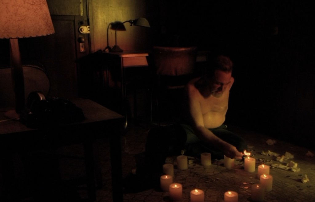 Philip Gerard shirtless on a motel floor with twelve candles in a circle
